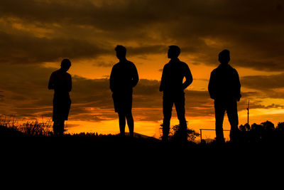 Silhouette young friends standing on field against orange sky