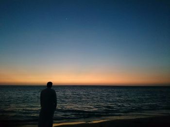 Silhouette of woman standing on beach at sunset