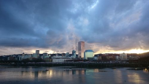 City at waterfront against cloudy sky