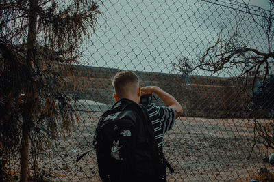 Rear view of man standing by chainlink fence