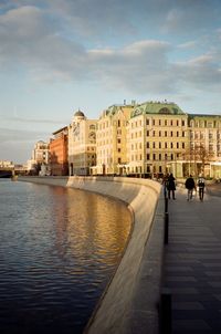 People walking by buildings in city against sky