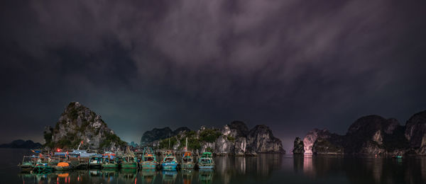 Boats moored on sea against cloudy sky at night