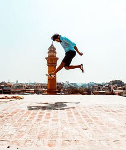 Man jumping by historic building in city against clear sky