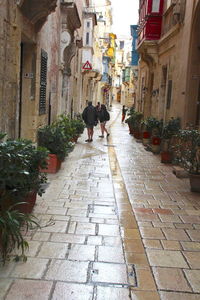 Rear view of woman walking on footpath amidst buildings in city