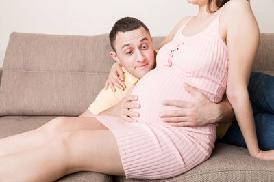 Midsection of friends sitting on sofa at home