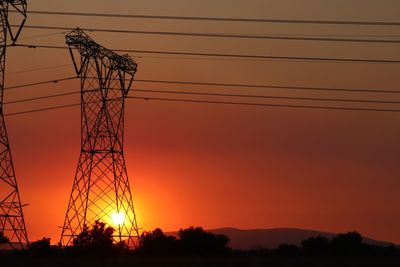 Low angle view of electricity pylon against sky during sunset