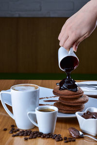 Cropped hand pouring chocolate sauce on cookies