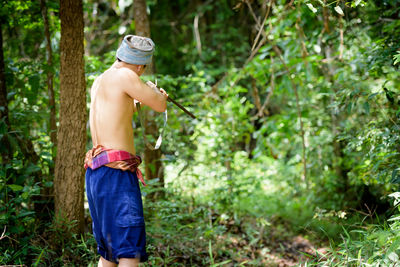 Full length of shirtless man standing in forest