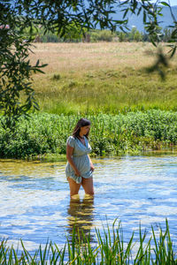 Girl wearing sundress, walking knee deep in creek on a hot day in summer