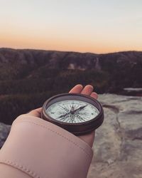 Close-up of hand holding clock against the sky