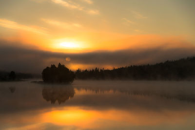 Trees reflection in lake against sky during foggy weather