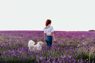 Rear view of woman standing with dog on field against sky