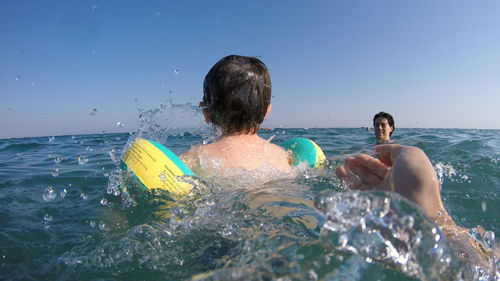 Father and son swimming in sea against clear sky