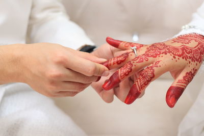 Midsection of groom holding bride finger on sofa during wedding