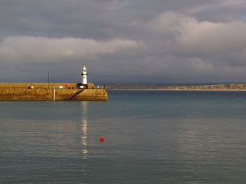 Lighthouse by sea against sky during sunset