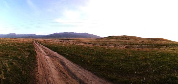 Dirt road amidst field against sky
