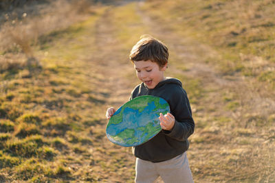 Portrait of cute boy holding globe against sky