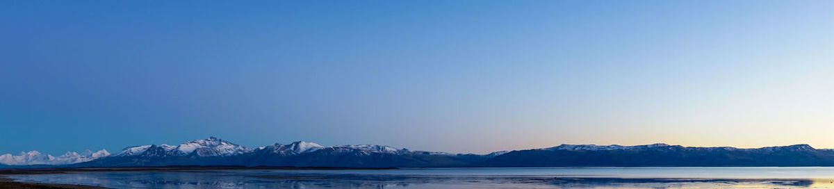 Scenic view of sea and snowcapped mountains against clear blue sky