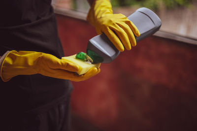 Caucasian male builder in yellow gloves squeezes detergent onto a sponge.