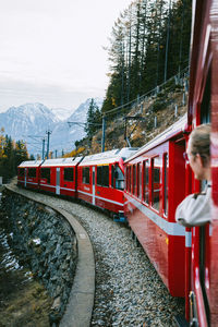 Red train in mountains, man looking through the window