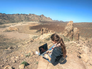 Teenage girl using laptop while sitting on rock at desert