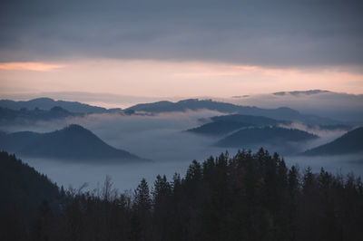 Scenic sunset view of silhouette mountains with fog in the valleys