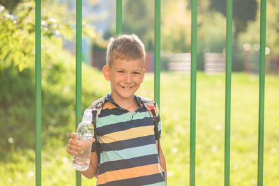 Portrait of smiling boy holding water bottle while standing outdoors
