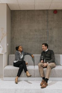 Full length of happy male and female delegates sitting on sofa discussing during seminar