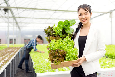 Portrait of a smiling young woman standing in greenhouse