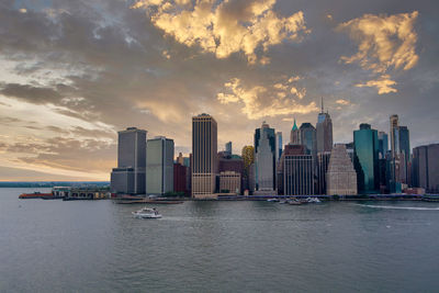 Sea by modern buildings against sky during sunset