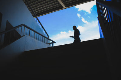 Low angle view of silhouette man standing on staircase against building