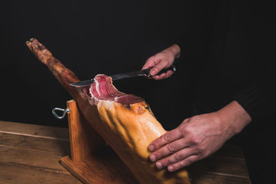 Closeup chef cutting ham with a knife on a wooden table on a black background