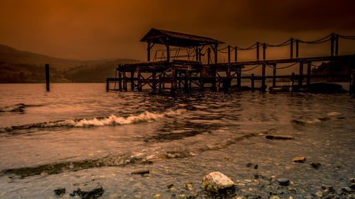 Pier on beach against sky during sunset