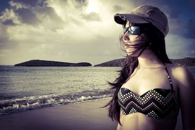 Teenage girl wearing bikini top and cap at beach against sky