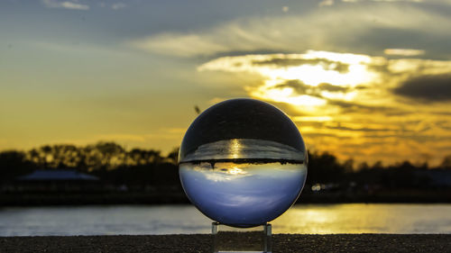 Close-up of crystal ball against lake during sunset