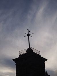 Low angle view of weather vane against cloudy sky