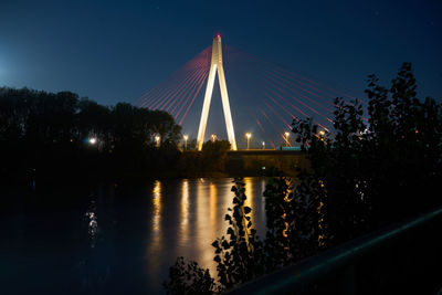 Illuminated bridge over river against sky at night