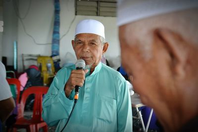 Senior man using microphone while standing indoors