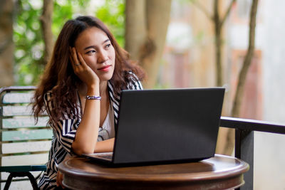 Thoughtful young woman sitting by laptop 