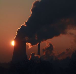 Low angle view of silhouette factory against sky during sunset