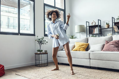 Happy young woman wearing headphones dancing at home