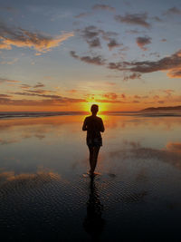 Rear view of silhouette woman standing in sea against sky during sunset