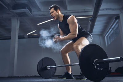 Motivated weightlifter clapping hands before barbell workout at gym