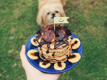 Cropped image of person holding fresh chocolate sauce on banana pancake in plate