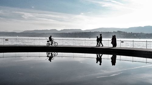 Reflection of silhouette people in lake against sky