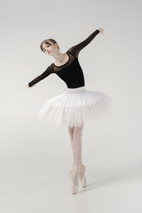 A ballerina in a bodysuit and tutu poses in motion showing ballet elements while standing on pointes