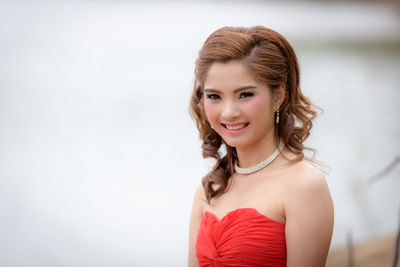 Portrait of beautiful young woman in dress standing against lake