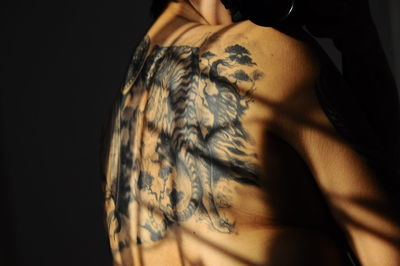 Midsection of man back with tattoo in darkroom