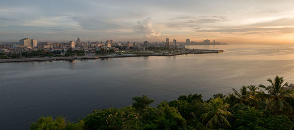 Panoramic view of city by sea against sky during sunset