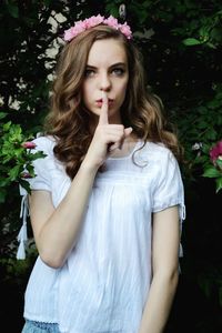 Portrait of beautiful woman wearing flowers with finger on lips by plants